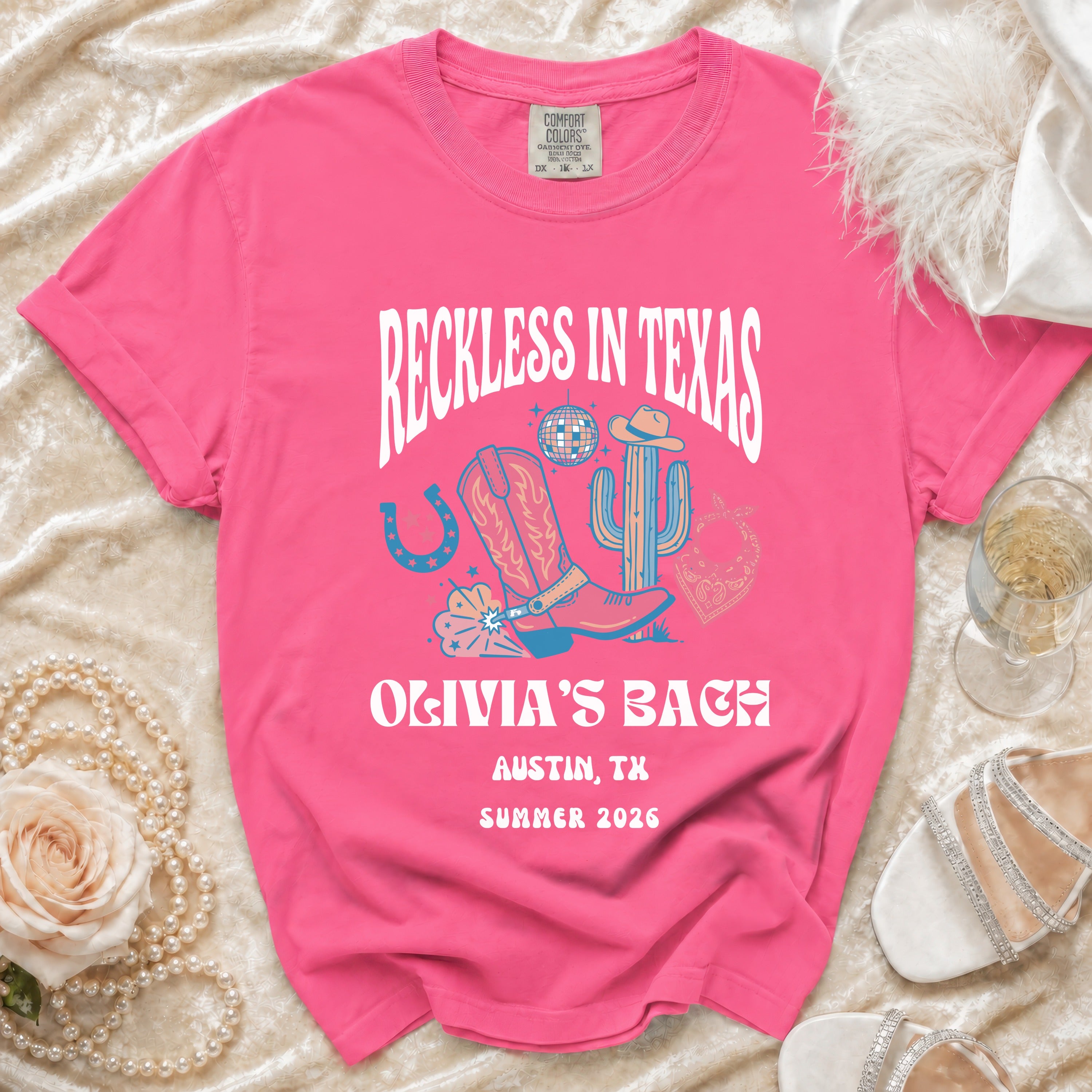 Pink t-shirt with "Reckless in Texas Olivia's Bach Austin, TX Summer 2026" graphic.