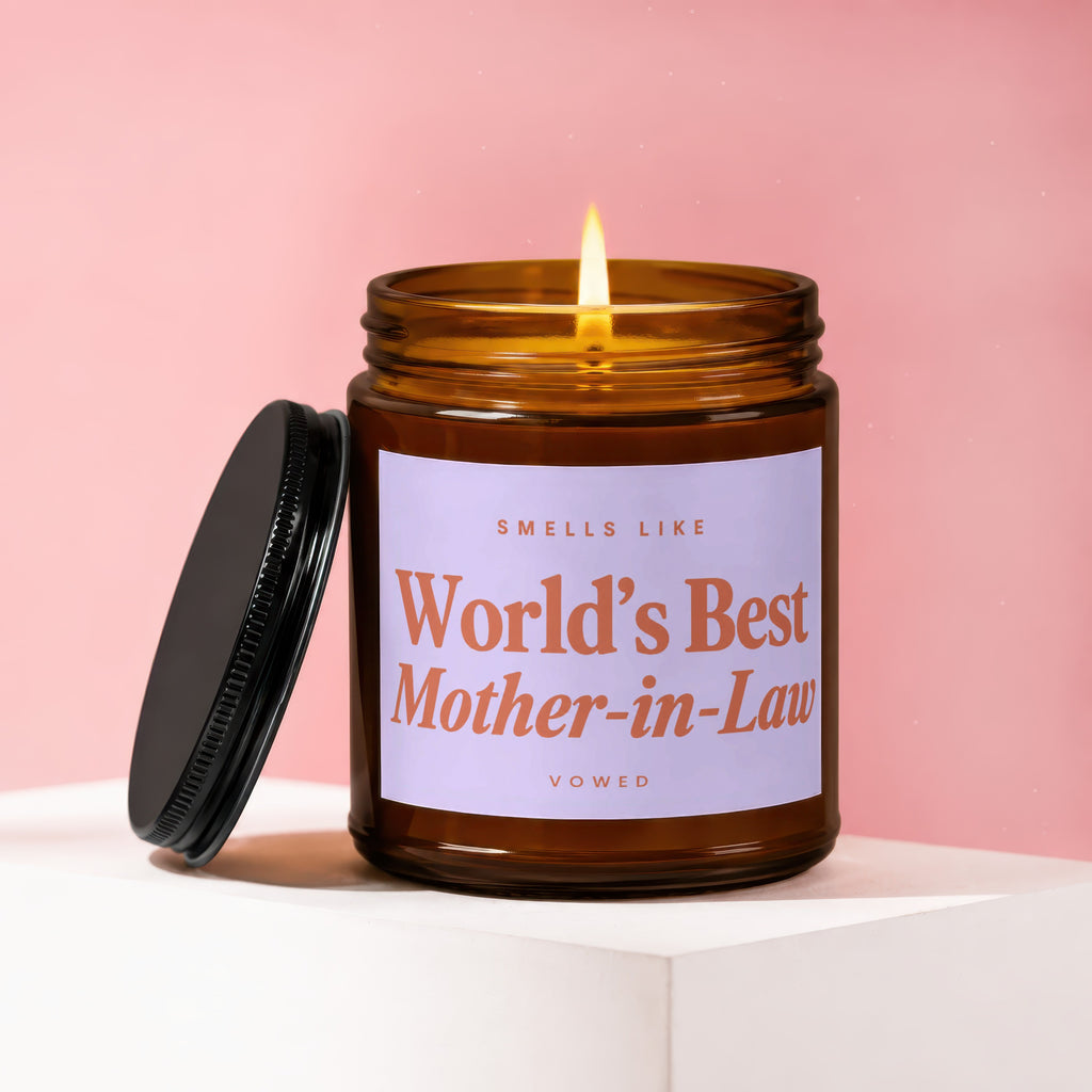 Amber candle with lit wick, lid beside it, label reads "Smells Like World's Best Mother-in-Law".