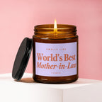 Amber candle with lit wick, lid beside it, label reads "Smells Like World's Best Mother-in-Law".