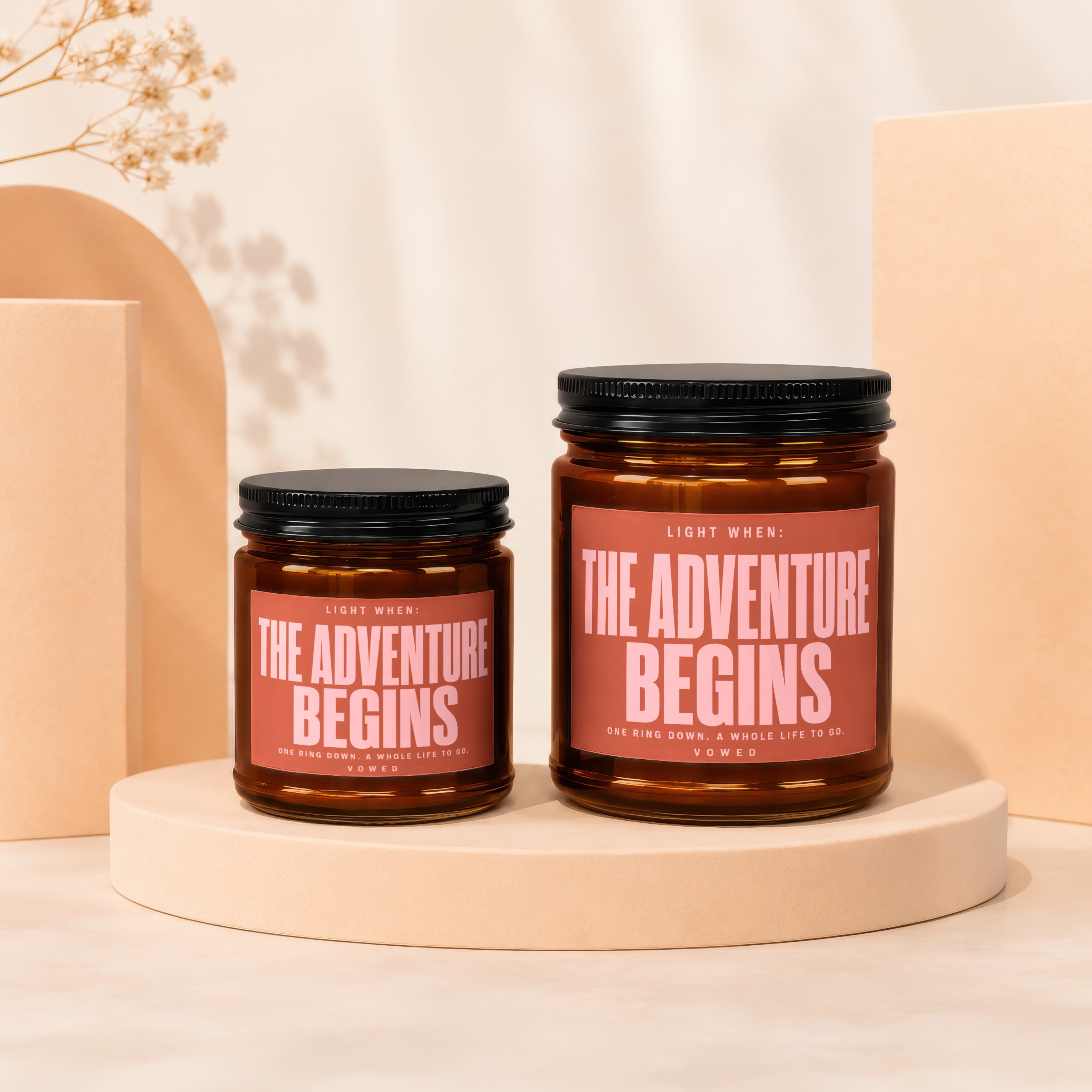 Two amber glass candles with "The Adventure Begins" printed on their labels.