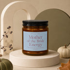 Amber glass candle labeled "Mother of the Bride Energy" with decorative elements.