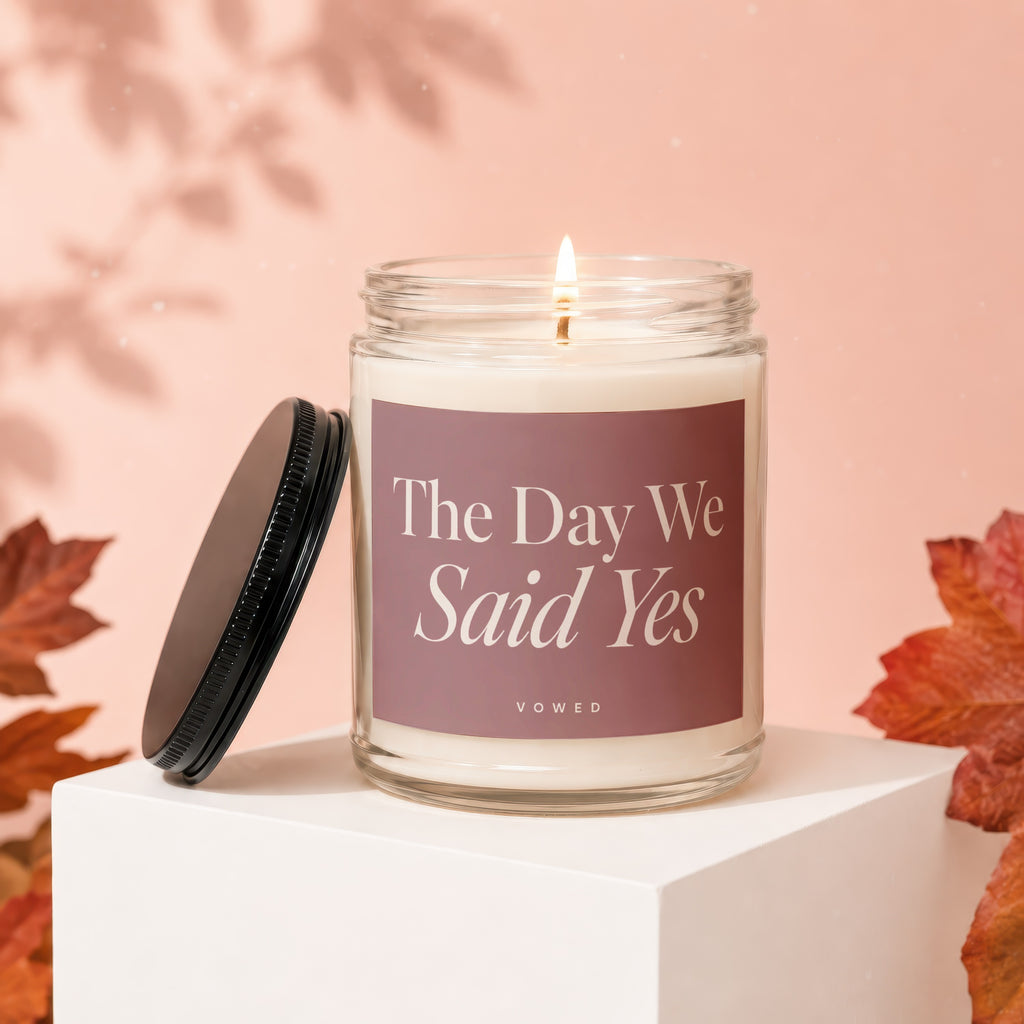 Glass jar candle with "The Day We Said Yes" text, lid off, autumn leaves accent.