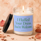 Glass candle, lit flame, blue label with green text "I Fluffed Your Dress. You're Welcome. VOWED."