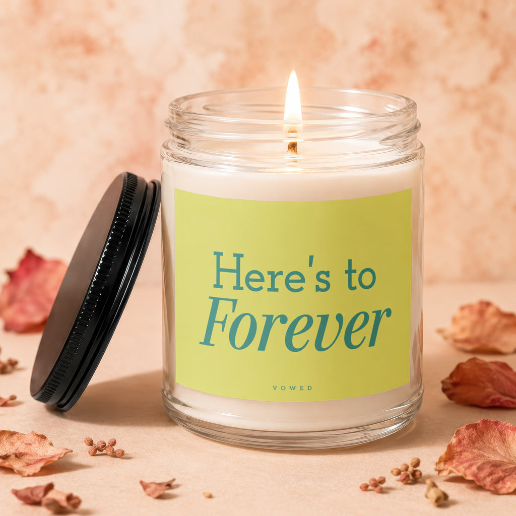 Scented candle with a lit wick and a "Here's to Forever" label.