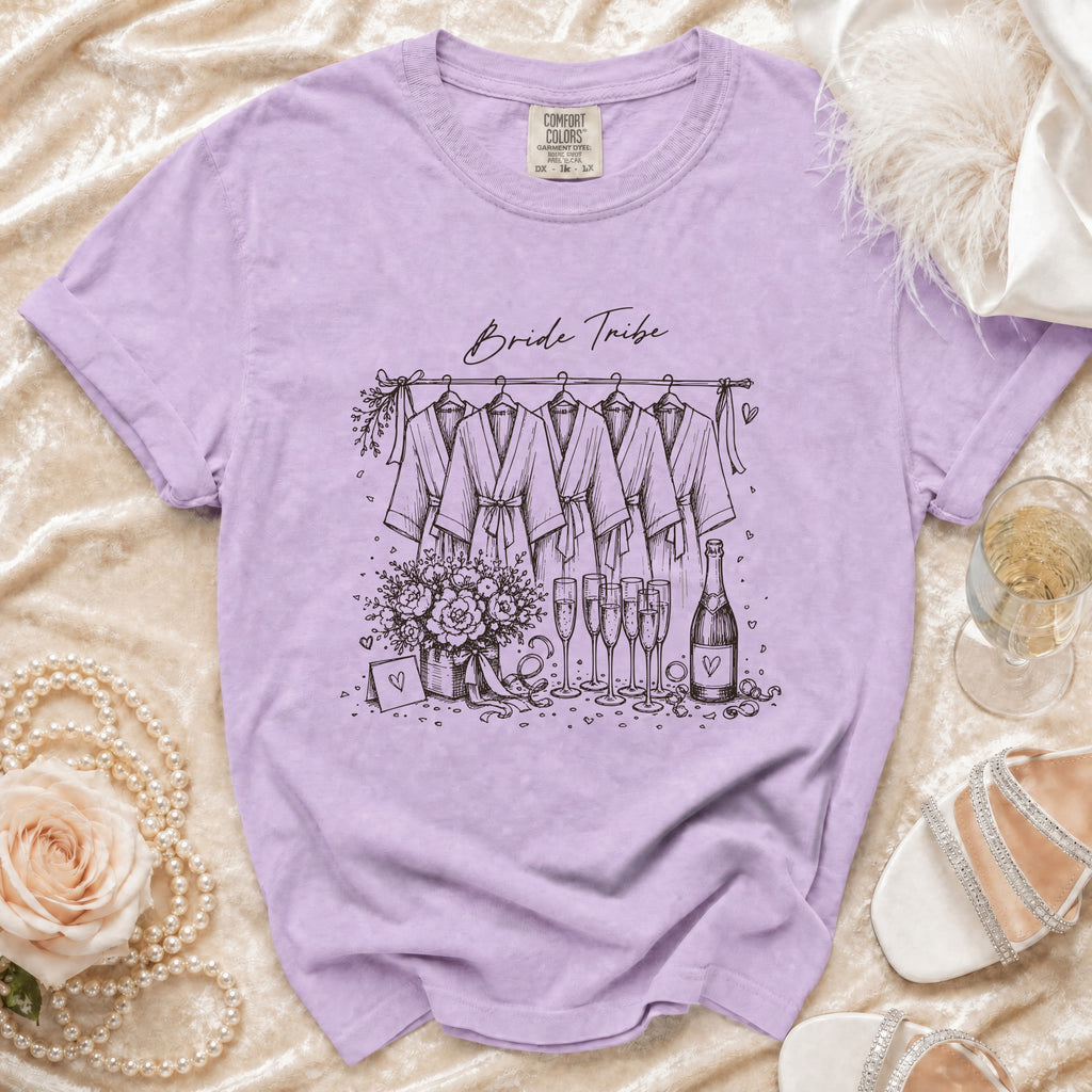 Lavender t-shirt with "Bride Tribe" graphic showing robes, flowers, champagne, and accessories.