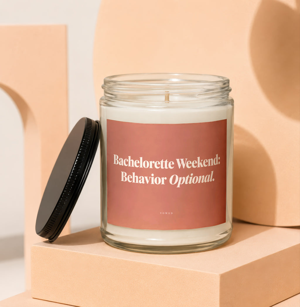 Glass candle with pink label reading "Bachelorette Weekend: Behavior Optional."