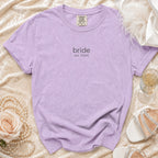 Purple t-shirt with 'bride est. 2026' text, flat lay with bridal accessories.