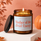 Burning amber glass candle with "Mother of the Bride Energy" label.