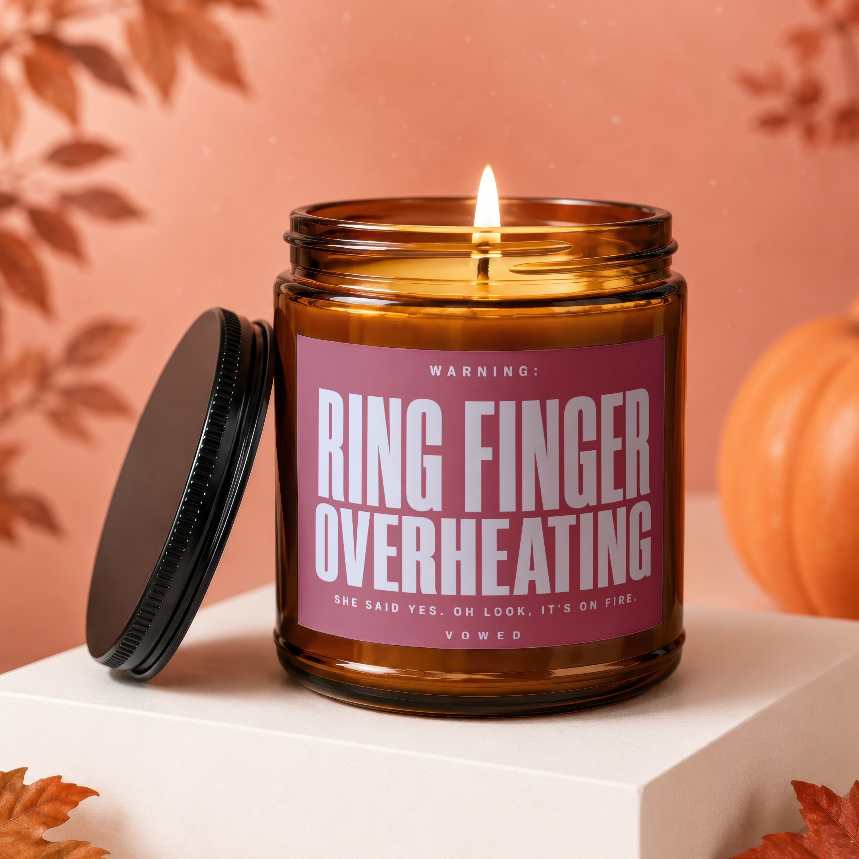 Amber jar candle with pink label reading "Ring Finger Overheating." Lid off.
