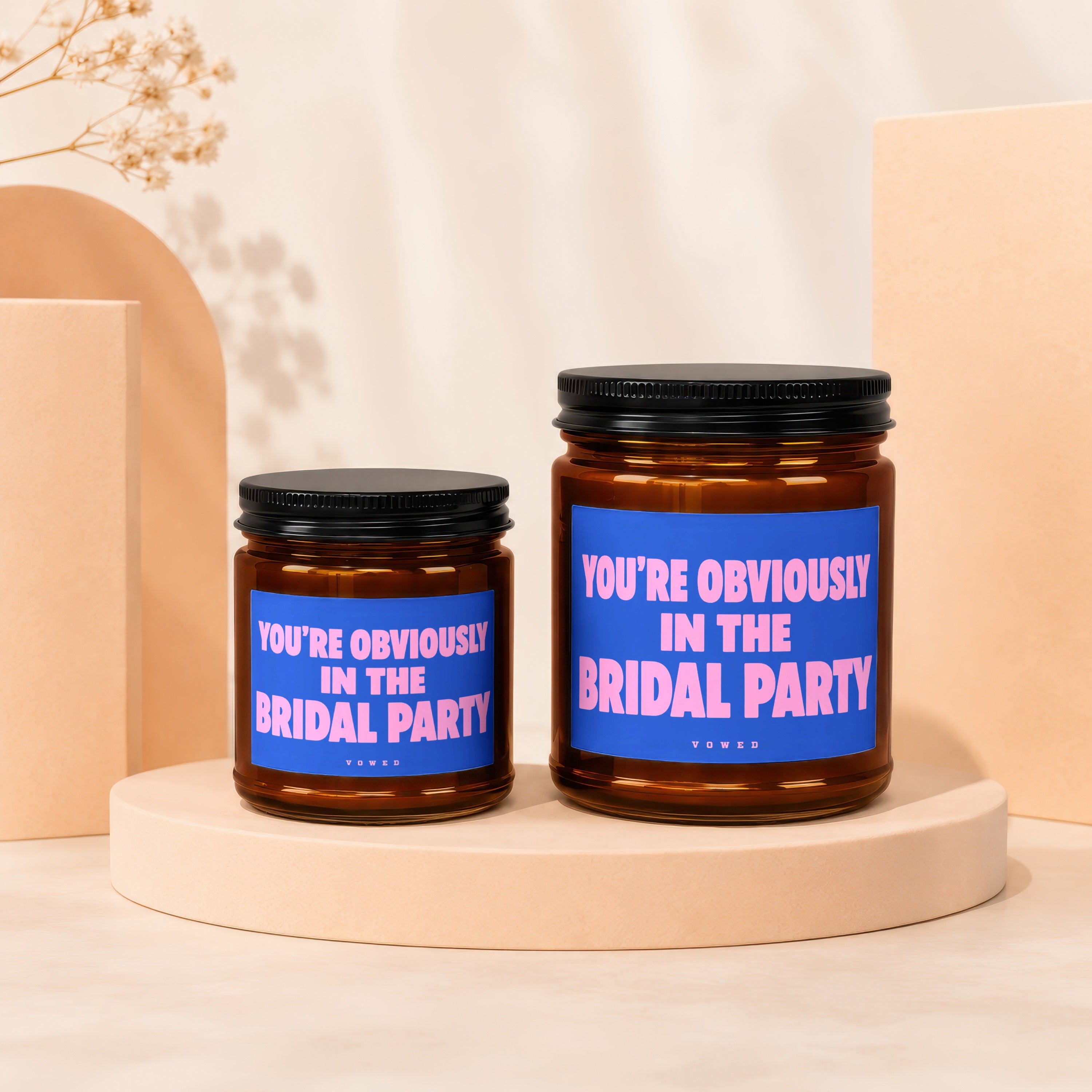 Two amber glass candles with black lids and blue labels reading "You're Obviously In The Bridal Party".