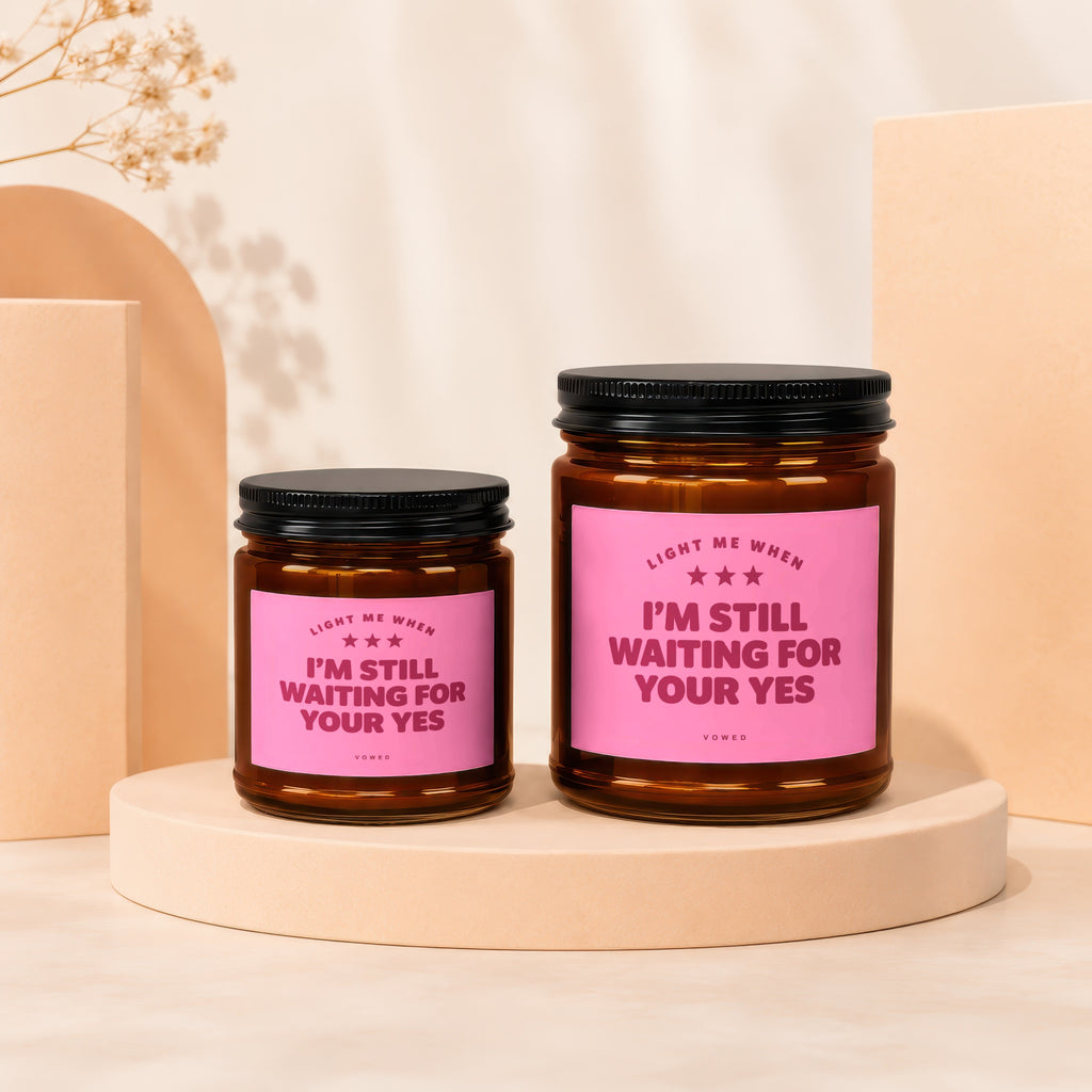 Two brown glass candles with pink labels that read "I'M STILL WAITING FOR YOUR YES."