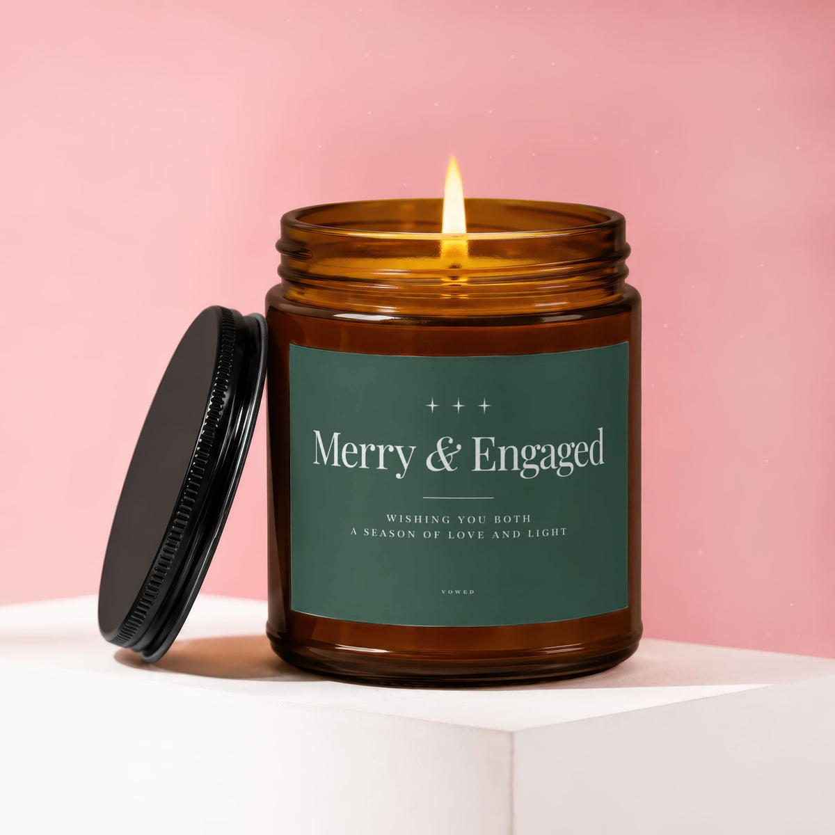 Amber jar candle with lit flame, green label reads "Merry & Engaged".
