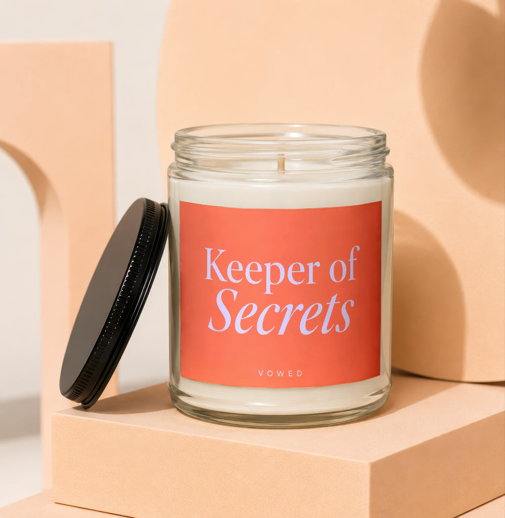 Glass jar candle with coral label that reads "Keeper of Secrets VOWED".