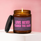 Amber jar candle with lit flame reads "Love Never Feared the Dark".