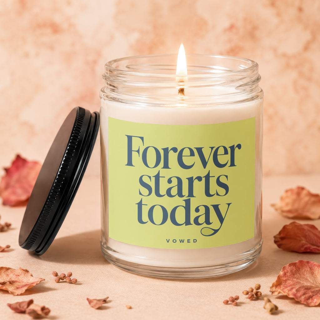Lit candle in glass jar with "Forever starts today" text on a light green label.