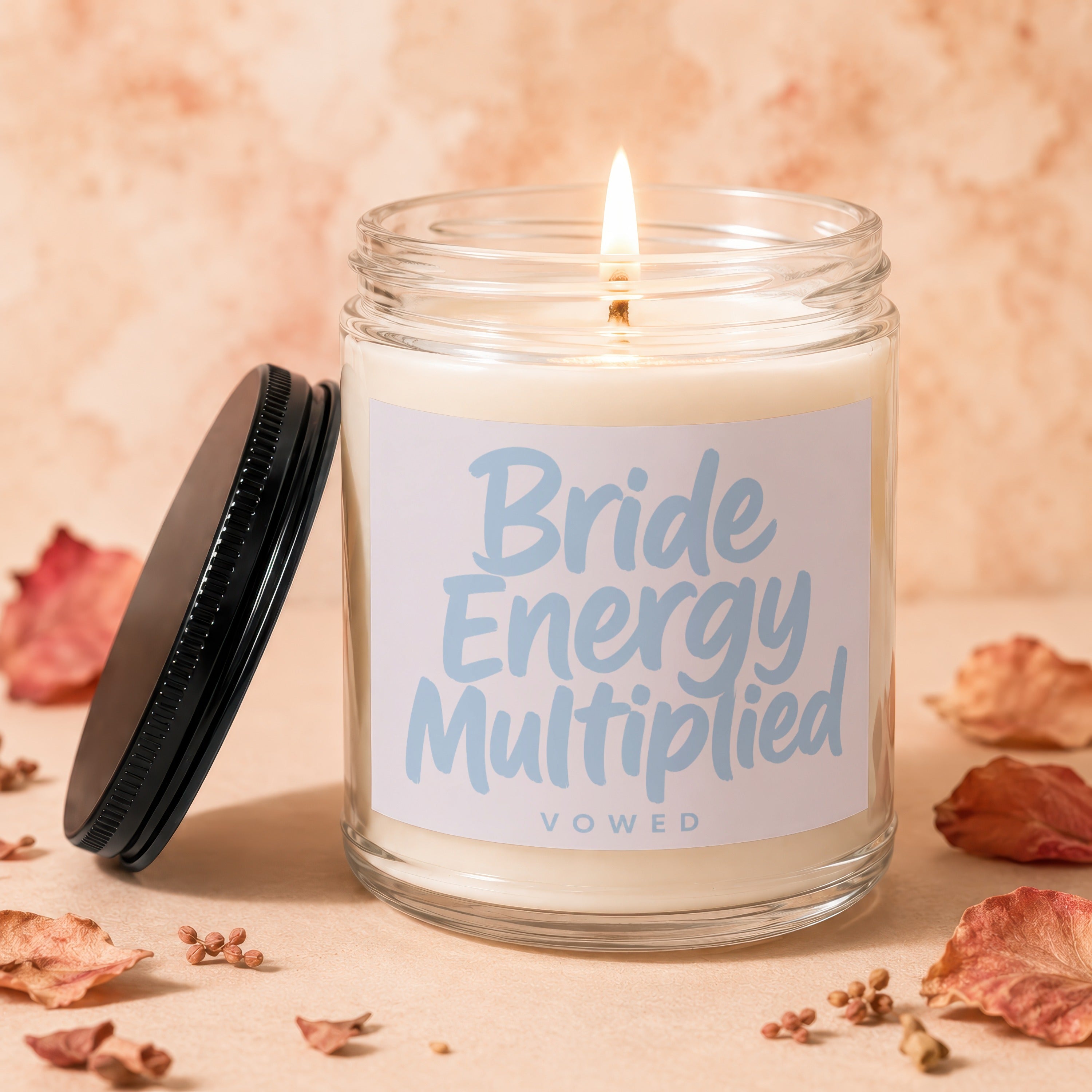 Candle with text "Bride Energy Multiplied Vowed" on label, lid off.