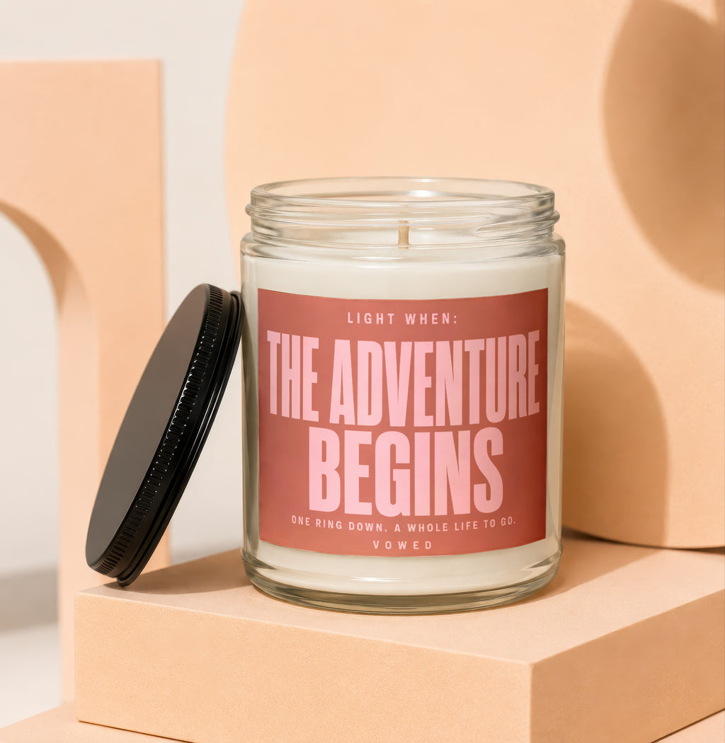 Glass candle with pink label reading "The Adventure Begins. One Ring Down."