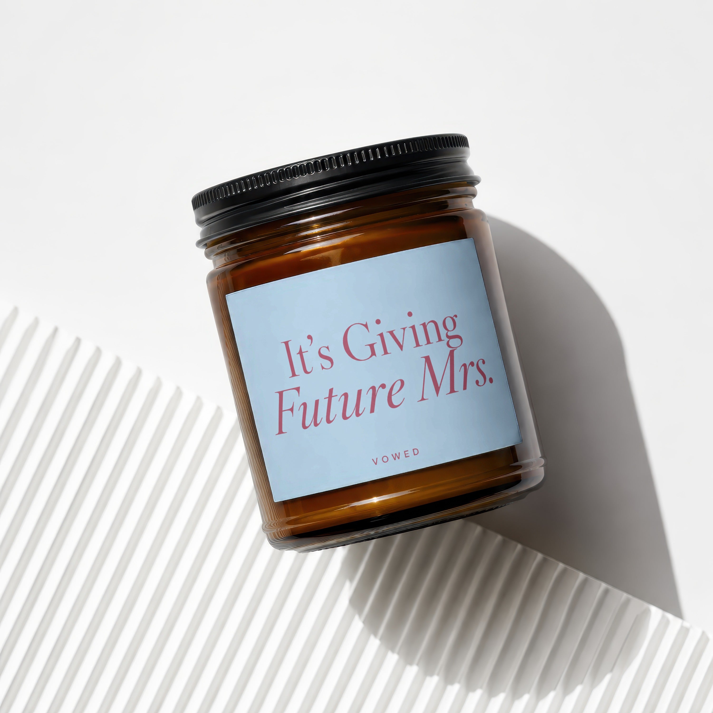 Amber glass candle with black lid, light blue label reading "It's Giving Future Mrs."
