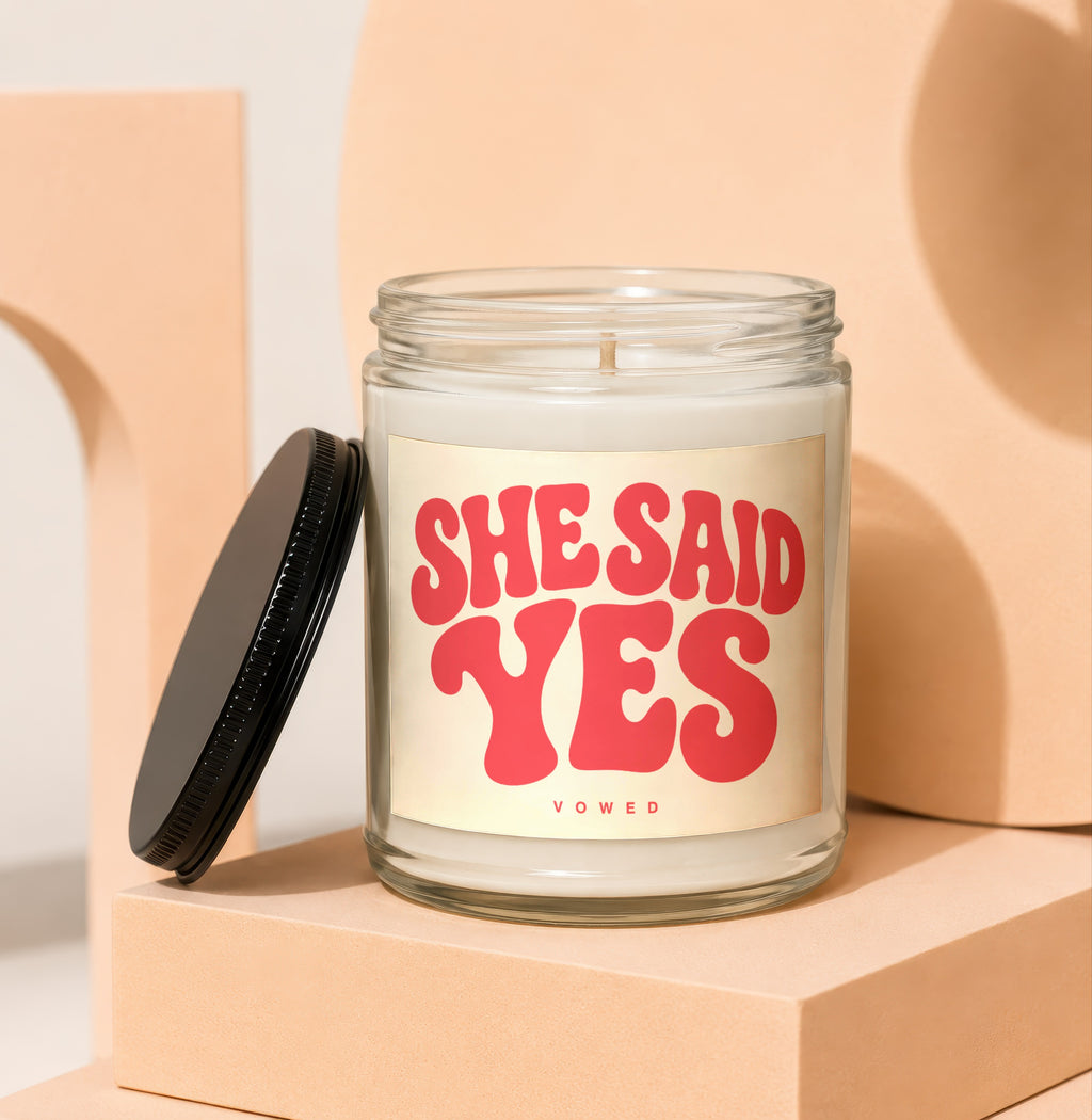 "She Said Yes" candle with red text on a cream label in a clear jar.
