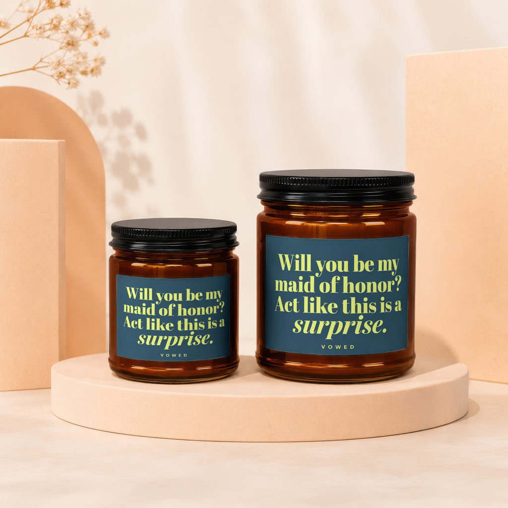 Two amber glass candles with dark lids display text asking "Will you be my maid of honor?"