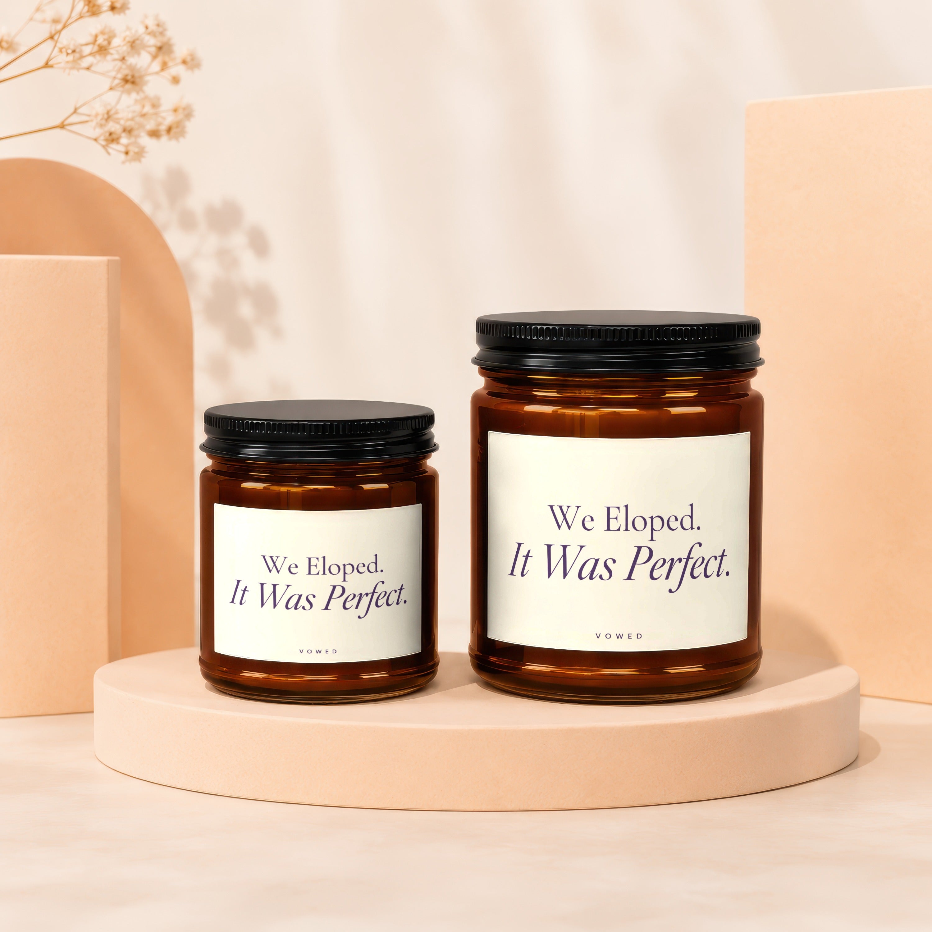 Two amber glass candles with black lids, labeled "We Eloped. It Was Perfect."