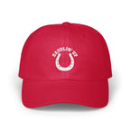 A red dad hat featuring white embroidery of a horseshoe and the text SADDLIN' UP.