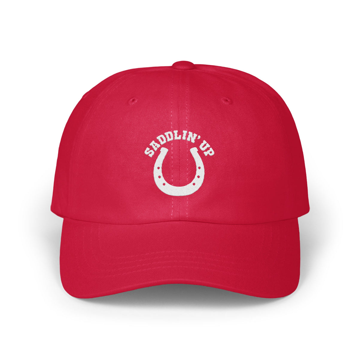 A red dad hat featuring white embroidery of a horseshoe and the text SADDLIN' UP.