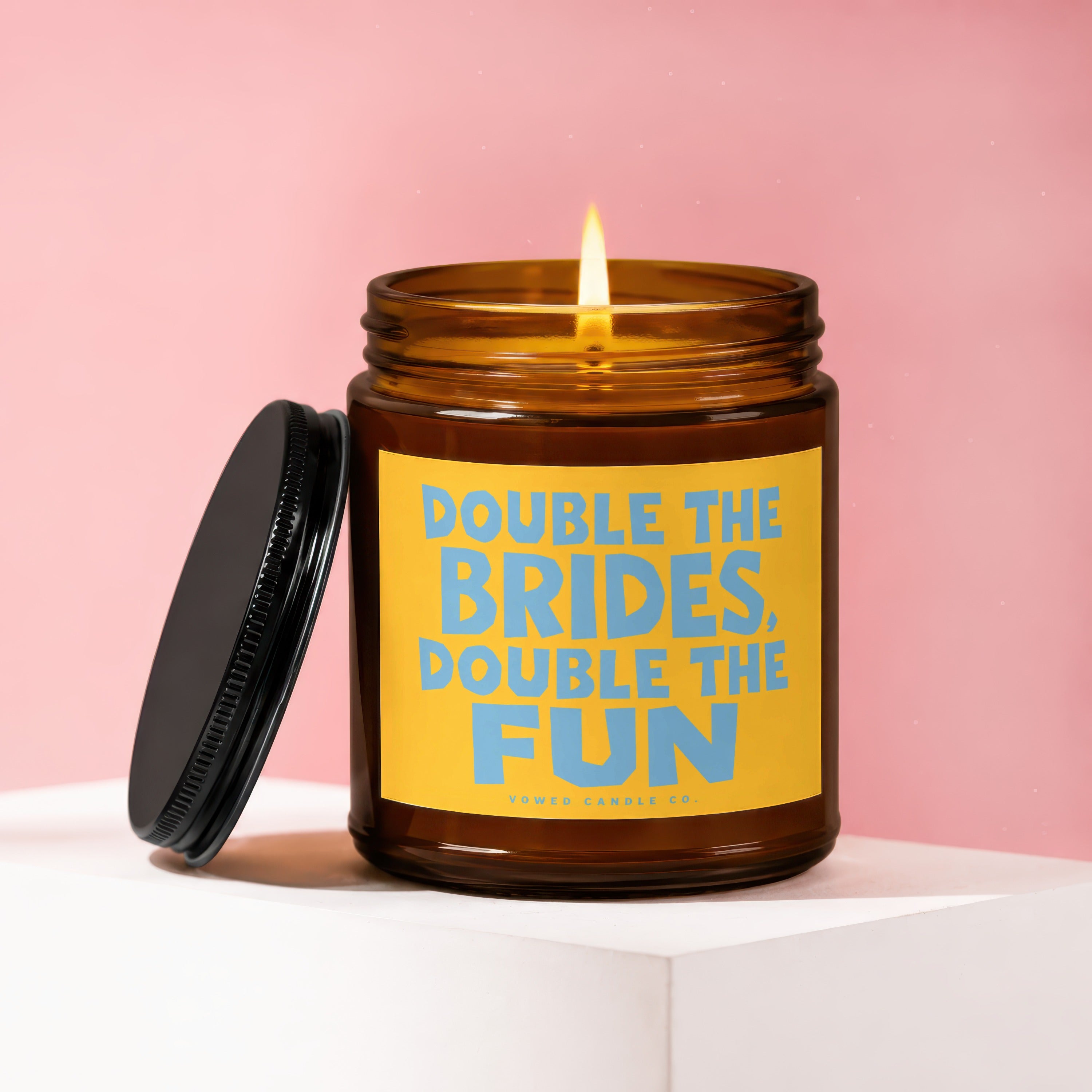 Brown glass candle with lit wick and yellow label reading "Double the Brides, Double the Fun".