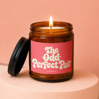 Amber jar candle with lit flame, red label reads "The Odd Perfect Pair".