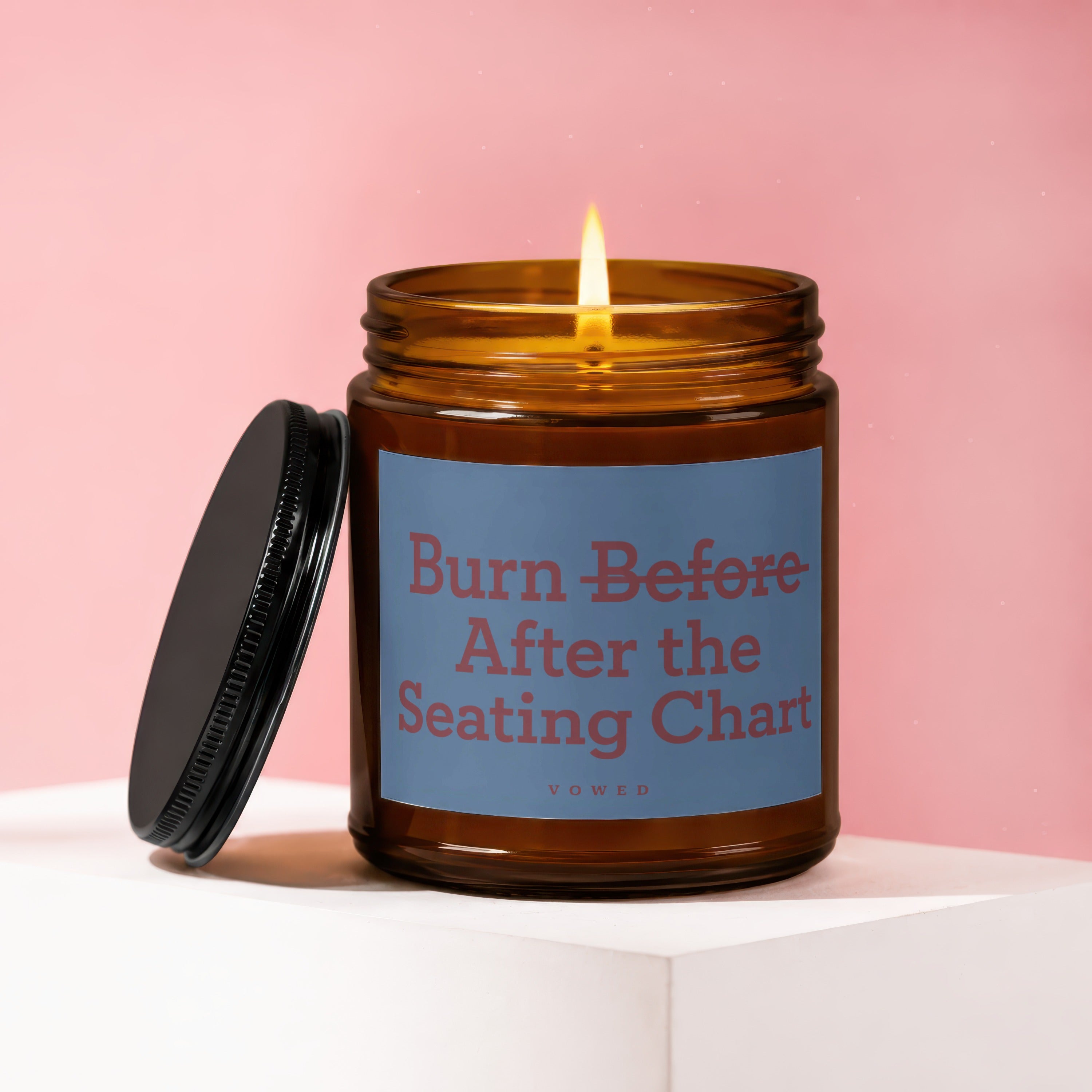Amber glass candle with lit wick and label reading "Burn Before After the Seating Chart".