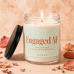 Glass candle with lit wick, "Engaged AF" and scent notes on label.