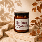 Amber jar candle labeled "The Coven Approves" with black lid and autumn decor.