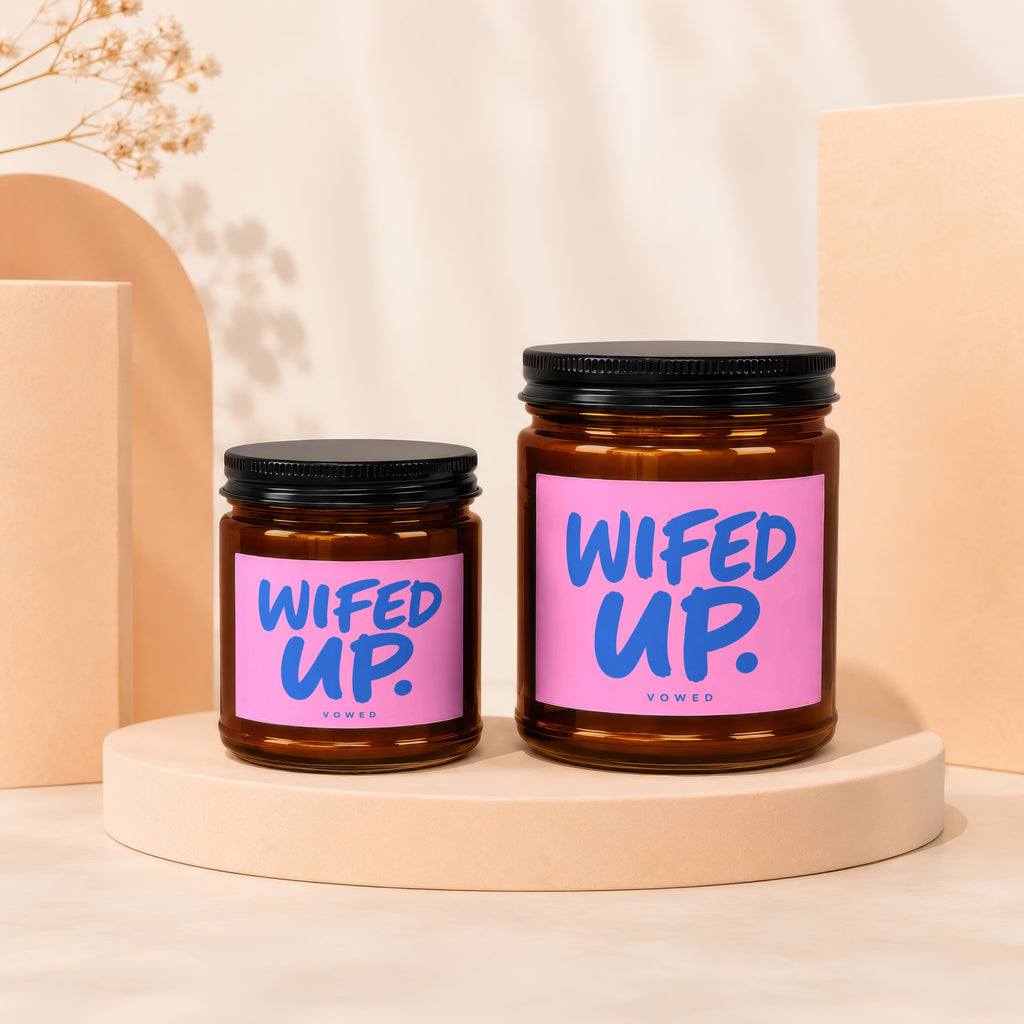 Two amber candles with pink labels that read "WIFED UP." and "VOWED"