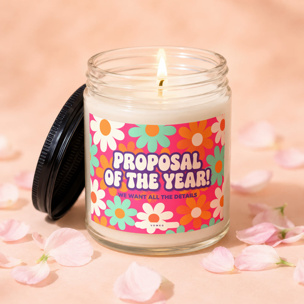 Lit candle in glass jar with "Proposal of the Year!" text and floral design.