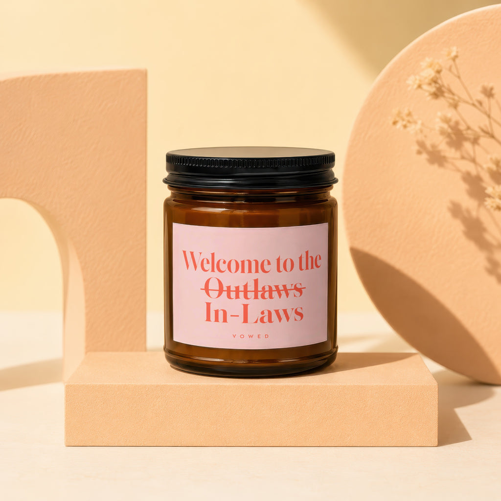 Amber candle with pink label reading "Welcome to the Outlaws In-Laws (vowed)".