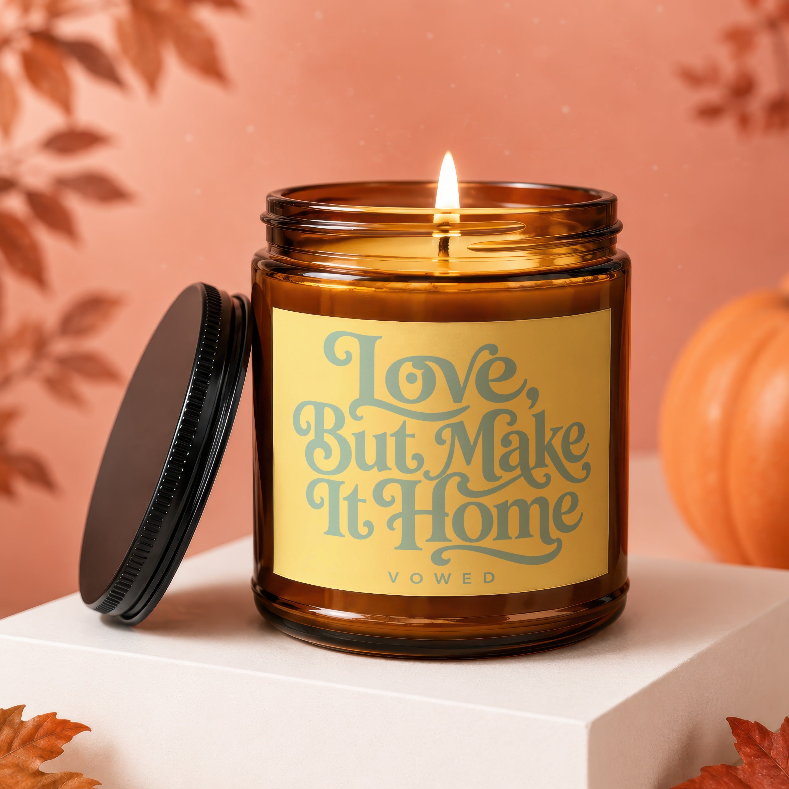 Amber jar candle with lit flame, yellow label reads "Love, But Make It Home VOWED".