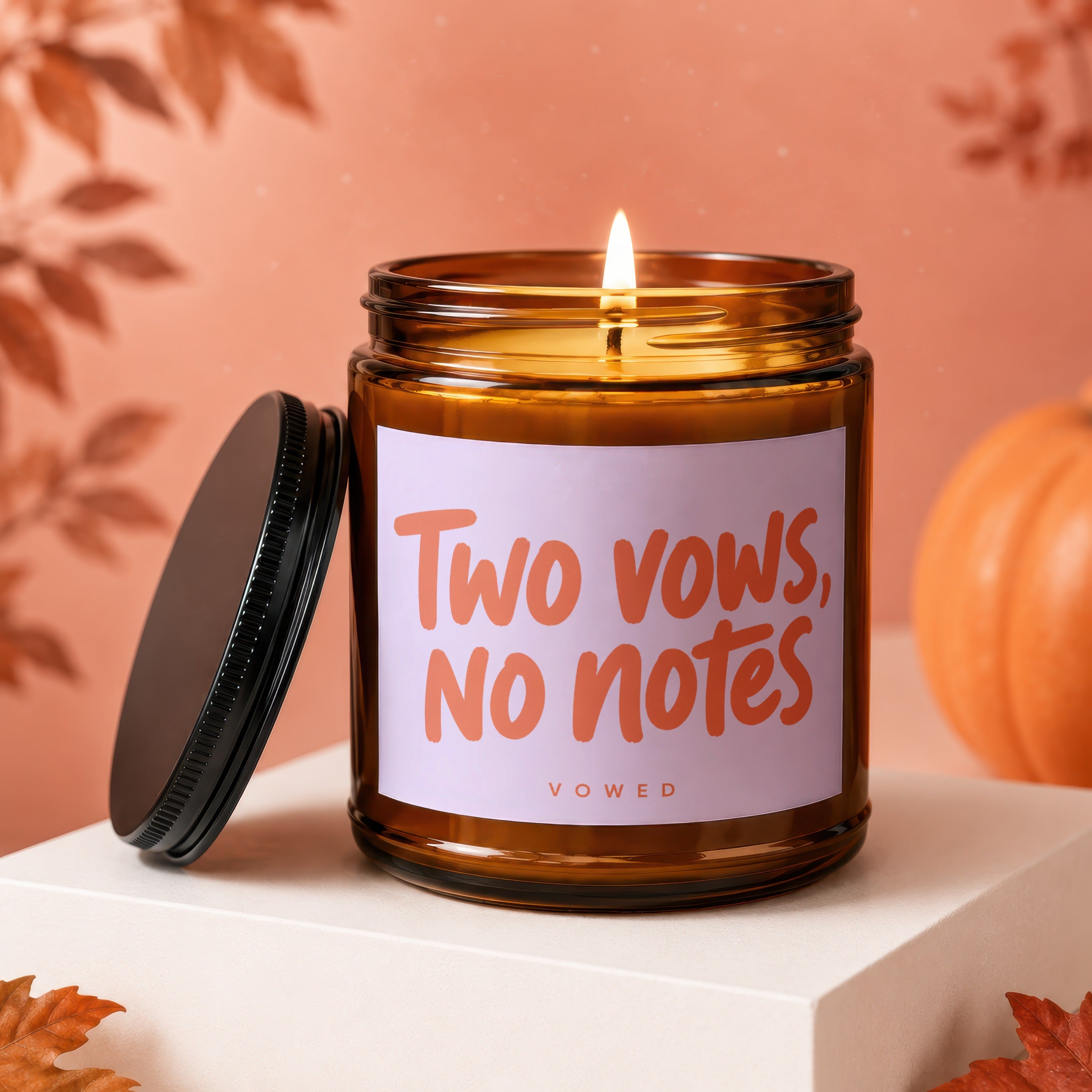 Amber candle with "Two vows, no notes" text, lid off, near pumpkin.
