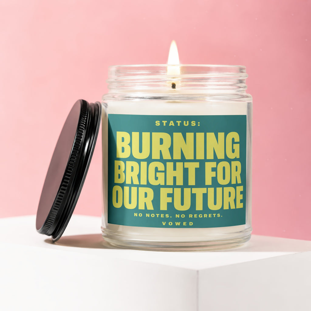 Glass candle with burning wick and teal label reading "Burning Bright for Our Future".