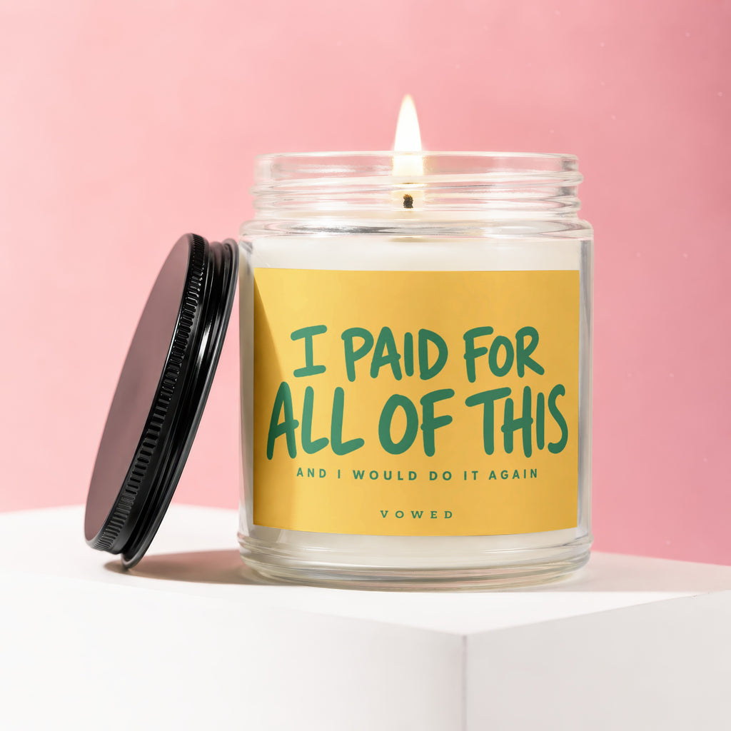 Glass candle in jar with lit wick and lid nearby, reads "I PAID FOR ALL OF THIS AND I WOULD DO IT AGAIN".