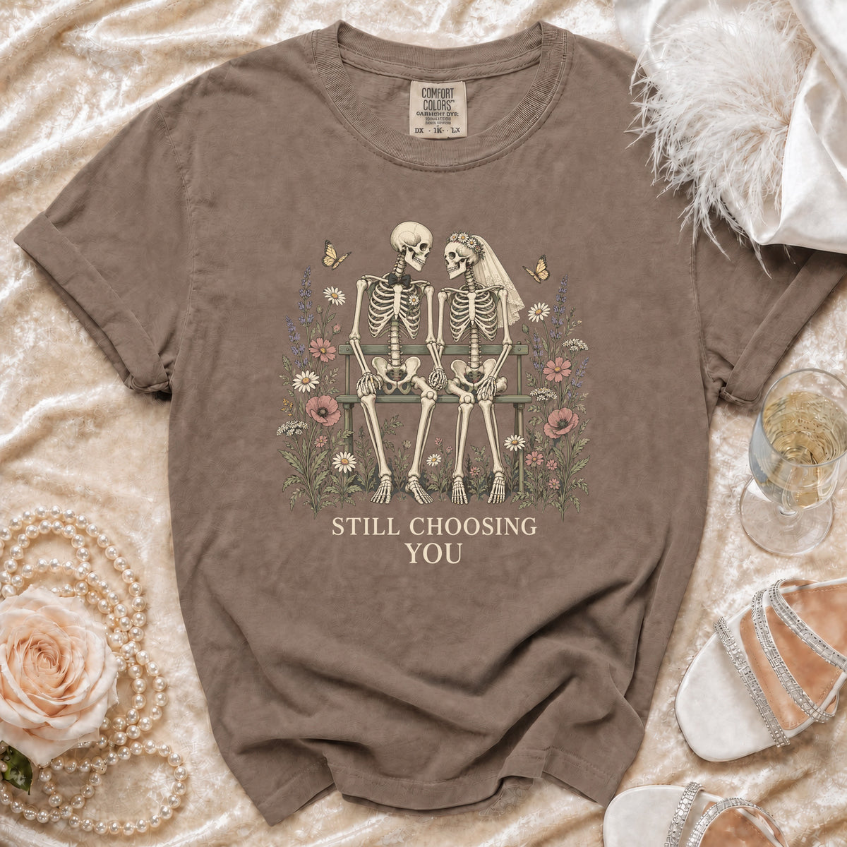 Skeleton couple on a bench surrounded by flowers, text "STILL CHOOSING YOU".