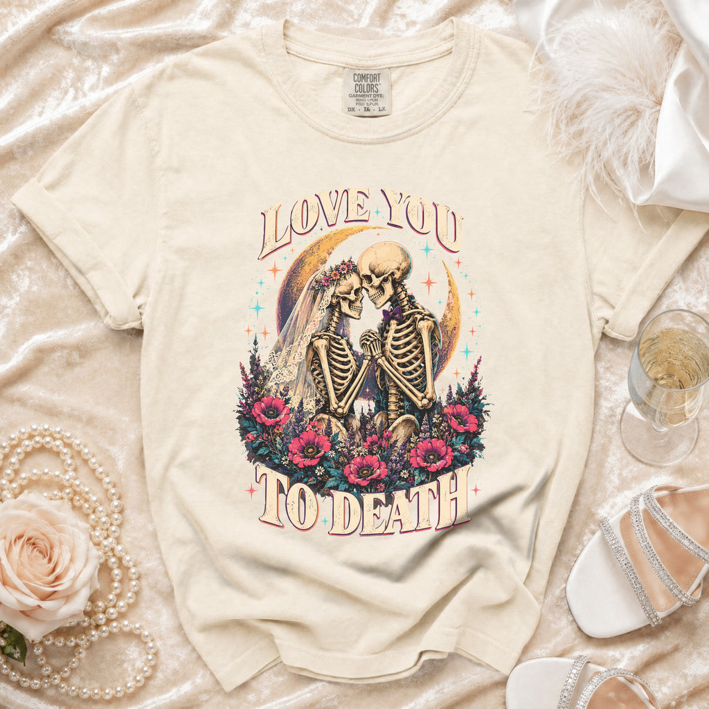Skeleton couple in wedding attire on a crescent moon with flowers and text "LOVE YOU TO DEATH".