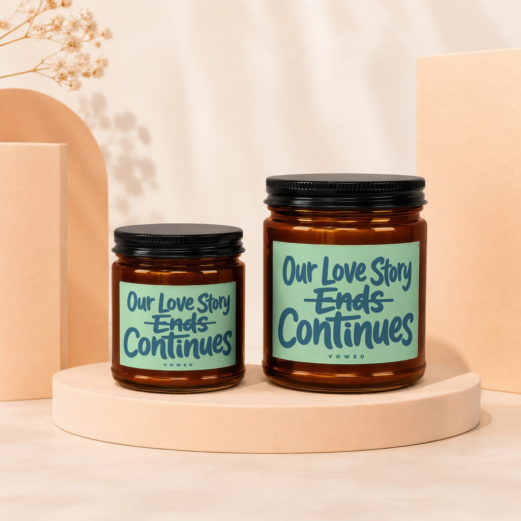 Two amber glass candles with black lids and mint green labels reading "Our Love Story Ends Continues".