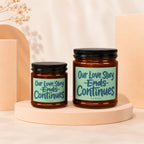 Two amber glass candles with black lids and mint green labels reading "Our Love Story Ends Continues".