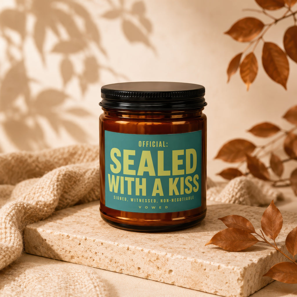 Amber jar candle with teal label reading "OFFICIAL: SEALED WITH A KISS"