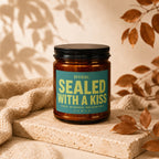Amber jar candle with teal label reading "OFFICIAL: SEALED WITH A KISS"