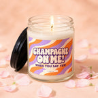 Glass candle with lit wick and a lid, featuring "Champagne on Me! When You Say Yes!" text.