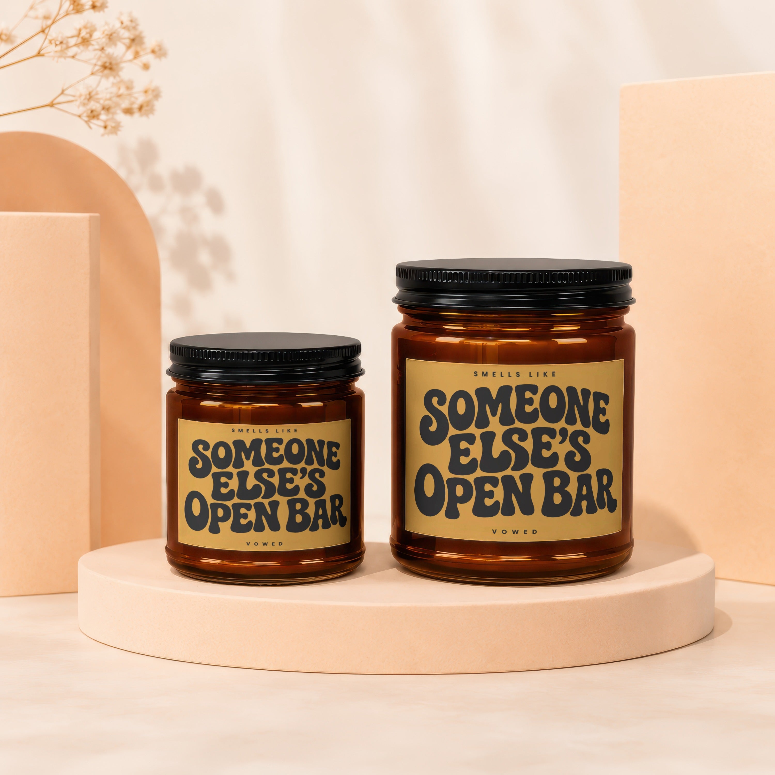 Two amber glass candles with black lids, featuring labels that read "Someone Else's Open Bar".