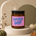 Brown glass candle with pink label reading "WIFED UP. VOWED".