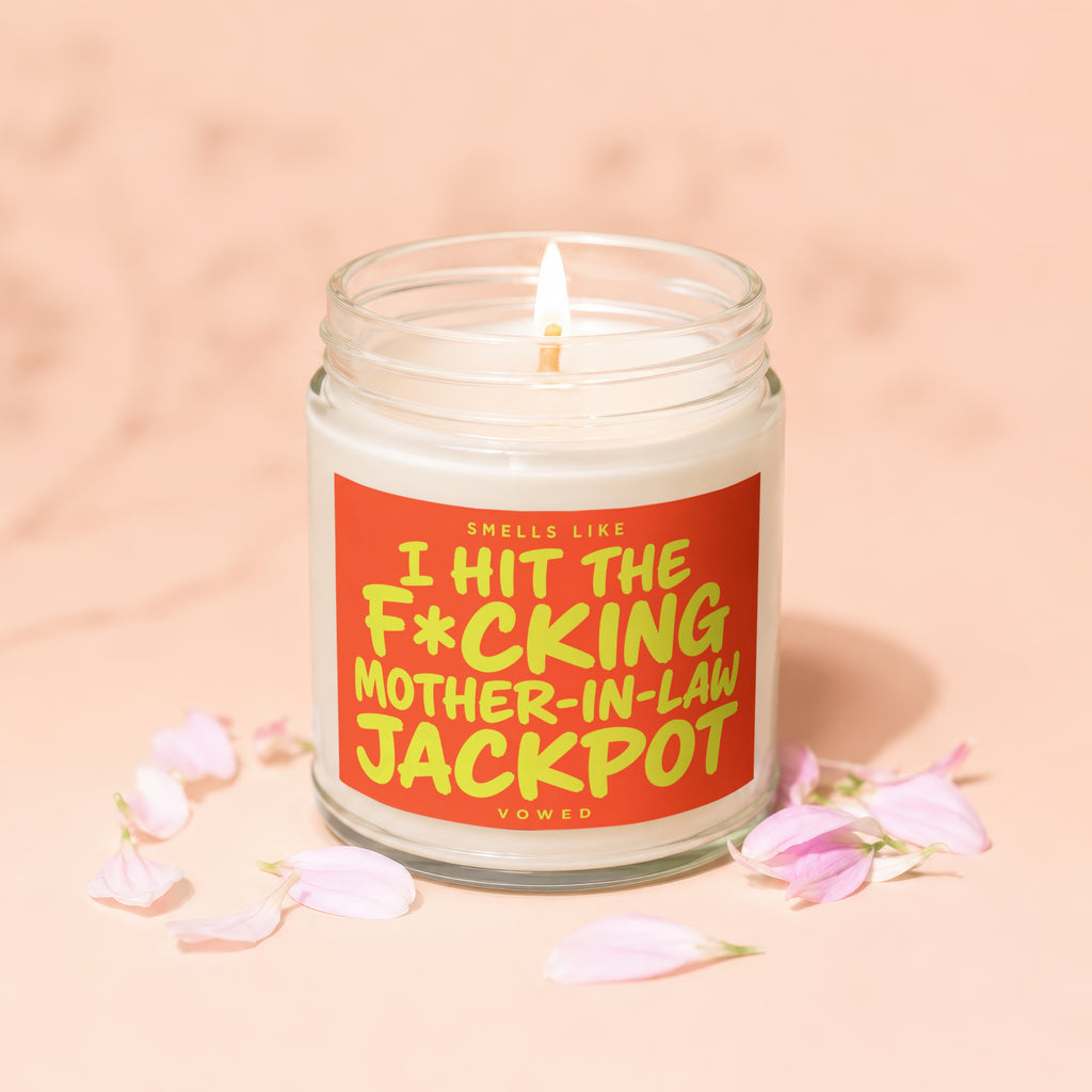 Lit candle in a jar with an orange label that reads "Smells Like I Hit the F*cking Mother-in-Law Jackpot."