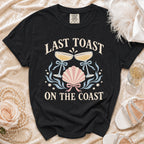 Black t-shirt with "Last Toast On The Coast" text and nautical graphics.